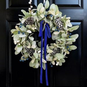 Winter wreath with frosted pinecones, blue berries, and velvet ribbon on black door