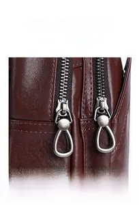 Detail of smooth silver metallic drop-shaped zippers on dark brown textured leather bag