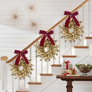 Golden leaf Christmas wreath with a red velvet bow hanging on a white indoor staircase