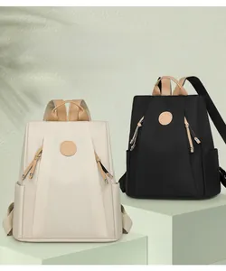 Detail of minimalist nylon backpacks in beige and black with leather accents on a pedestal