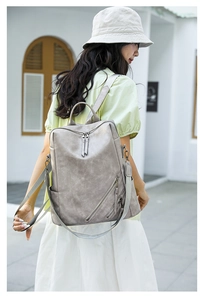 Outdoor view of a grey washed leather backpack with side zippers on a woman back