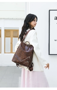 Detail view of brown leather checkerboard backpack with side zipper and tassel on a model
