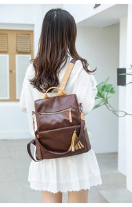 Detail of a dark brown leather backpack with tassels and multiple zipper compartments