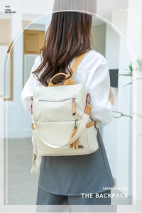 Detail of cream backpack featuring tan leather straps and stylish tassel accessory