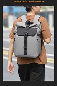 Outdoor street view of a grey roll-top travel backpack with black straps and buckle