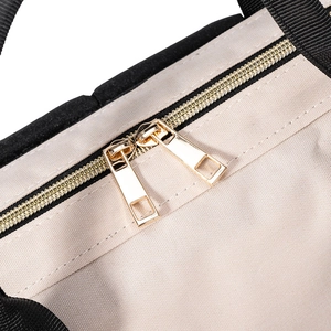 Détails des doubles fermetures dorées et poignées noires sur le sac en toile beige