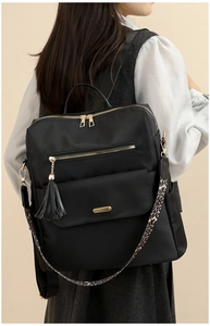 Detail of black backpack with gold zippers, tassel charm, and leopard print shoulder strap