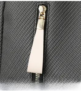 Close-up of golden metal zipper and long cream leather pull on woven grey backpack