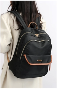 Back view of a large black travel backpack with brown leather trim and golden zippers