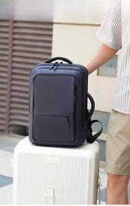Blue travel backpack detail showing side USB charging port and thick padded handle on a suitcase