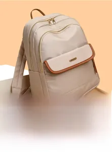 Detail of beige nylon backpack with brown leather trim and golden zippers in close-up view