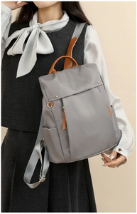 Detailed side view of grey canvas laptop backpack with brown leather accents on a model