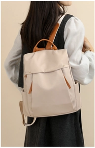 Detail view of the beige canvas backpack with premium tan leather handles and metal hardware