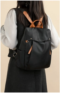 Detail view of stylish black canvas backpack with brown handles and gold hardware accents