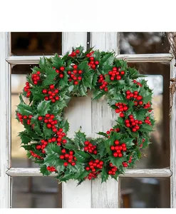 Detail eines Weihnachtskranzes mit grünen Blättern und roten Beeren am rustikalen Fenster