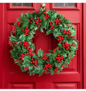 Detail von künstlichem Weihnachtskranz mit grünen Blättern und roten Beeren an Tür