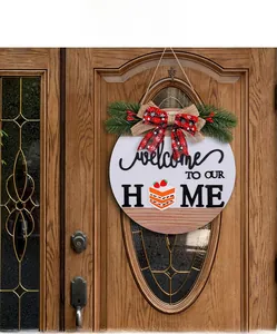 Detail of wooden welcome sign with buffalo plaid bow and greenery on a dark wood door