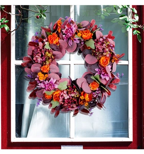Détail d'une couronne florale automnale suspendue à une fenêtre blanche sur mur rouge