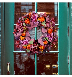 Gros plan d'une couronne d'automne avec roses oranges et baies sur porte verte