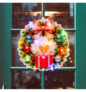 Luminous Christmas wreath with LED lights, orange bow and ornaments on a wooden window