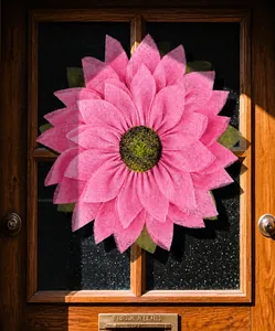 Detail of pink burlap sunflower wreath hanging on dark wooden glass door in warm sunlight
