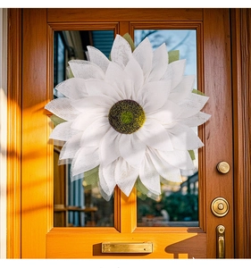 Close-up of a white burlap sunflower wreath hanging on a dark wooden front door