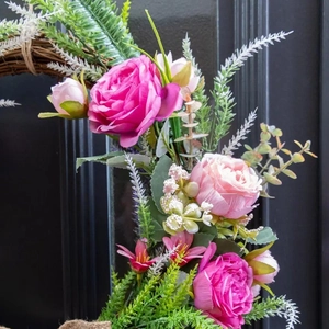 Artificial pink rose wreath with green leaves on a natural rattan base for home wall decor