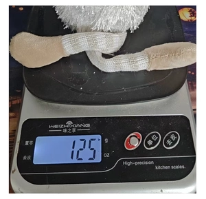 White plush Christmas tree toy with long legs being weighed on a scale, 125g weight