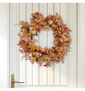 Dettaglio ghirlanda autunnale con foglie di acero e bacche su una porta di legno bianca