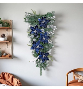 Blue glitter velvet poinsettia teardrop swag with snowy pine needles on a grey wall