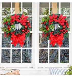 Detail of Christmas wreath with red poinsettia, berries, and LED lantern on window