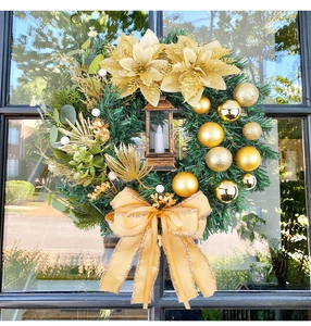 Detail of a Christmas wreath featuring golden silk flowers and a vintage lantern light