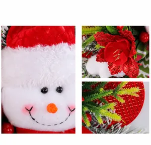 Détails d'un visage de bonhomme de neige en peluche, fleur rouge et branche de sapin enneigée