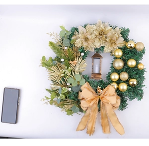Close-up of Christmas wreath with golden flowers, large bow, and vintage candle lantern