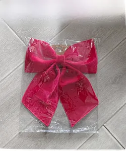 Detail of a large magenta velvet decorative bow in clear plastic packaging on a wood surface