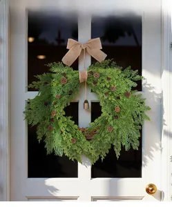 Close-up of heart-shaped wreath with pine cones, burlap bow, and vintage bell on door