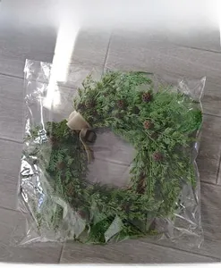 Christmas pine cone wreath with burlap bow detail shown in protective clear plastic packaging