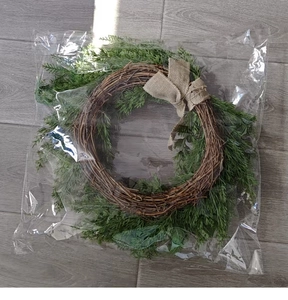 Detail of a Christmas wreath with pine needles and burlap bow in clear protective packaging