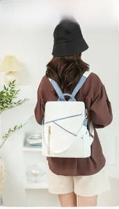 Minimalist white and blue backpack with golden zippers shown on a model in a home setting