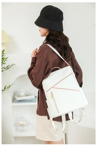 Side view of a white minimalist backpack with pink zippers worn by a model in a room