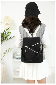 Detail of black nylon backpack with white straps and gold hardware on model