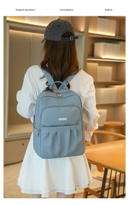 Detailed back view of a sky blue Oxford cloth backpack on a model in a warm room