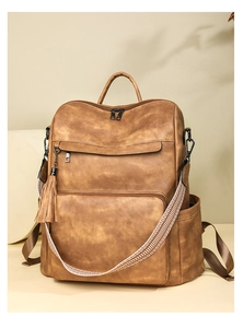 Detail of vintage brown leather backpack showing fringe tassel and woven strap accents