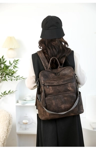 Close-up of vintage brown leather laptop backpack featuring side tassel and woven strap