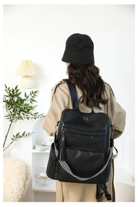 Detail of black leather backpack featuring tassel zippers and geometric woven shoulder strap