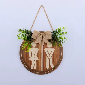 Close-up of circular wooden restroom sign with linen bow and green leaf accents