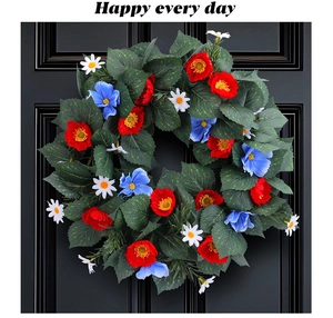 Detail of red and blue faux flowers on a green leaf wreath against a black door