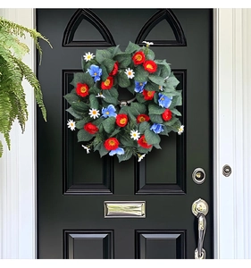 Close-up of red blue and white artificial flowers on a lush green foliage wreath on a black door