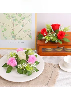 Detail view of pink rose candle ring with lush green leaves on a table setting