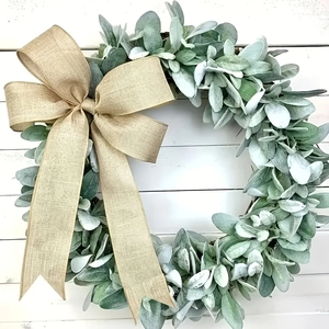 Detailed view of artificial lamb's ear wreath with a large burlap bow on white wood wall